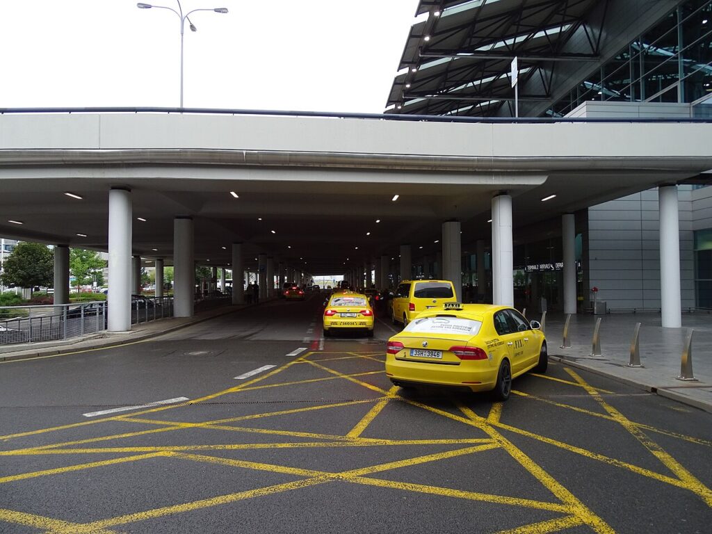 Žlutá taxi na vyhrazeném stanovišti pod přístřeškem před Terminálem 2 letiště Praha Ruzyně